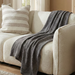 Beige sofa with a gray throw blanket and striped pillow in a living room setting.