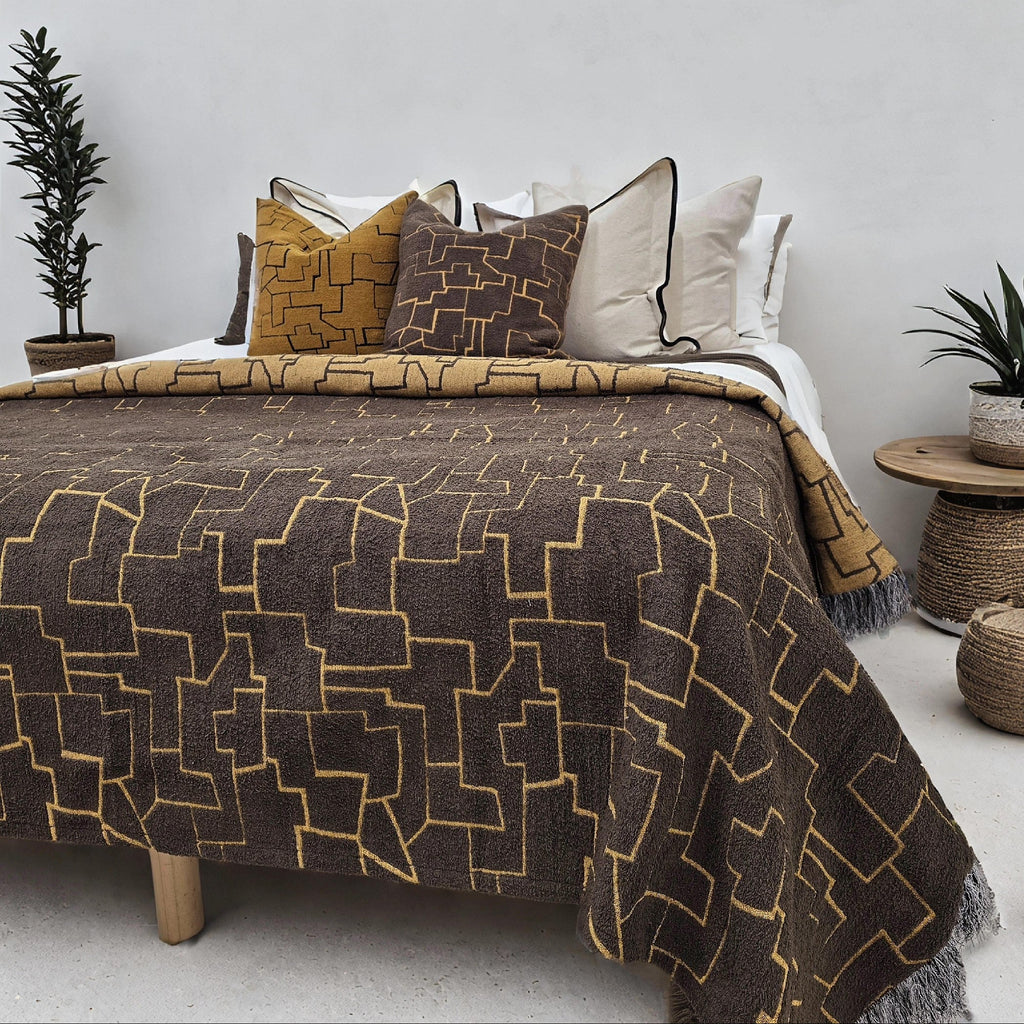 Bed with patterned brown and gold blanket and decorative pillows in a bedroom setting.