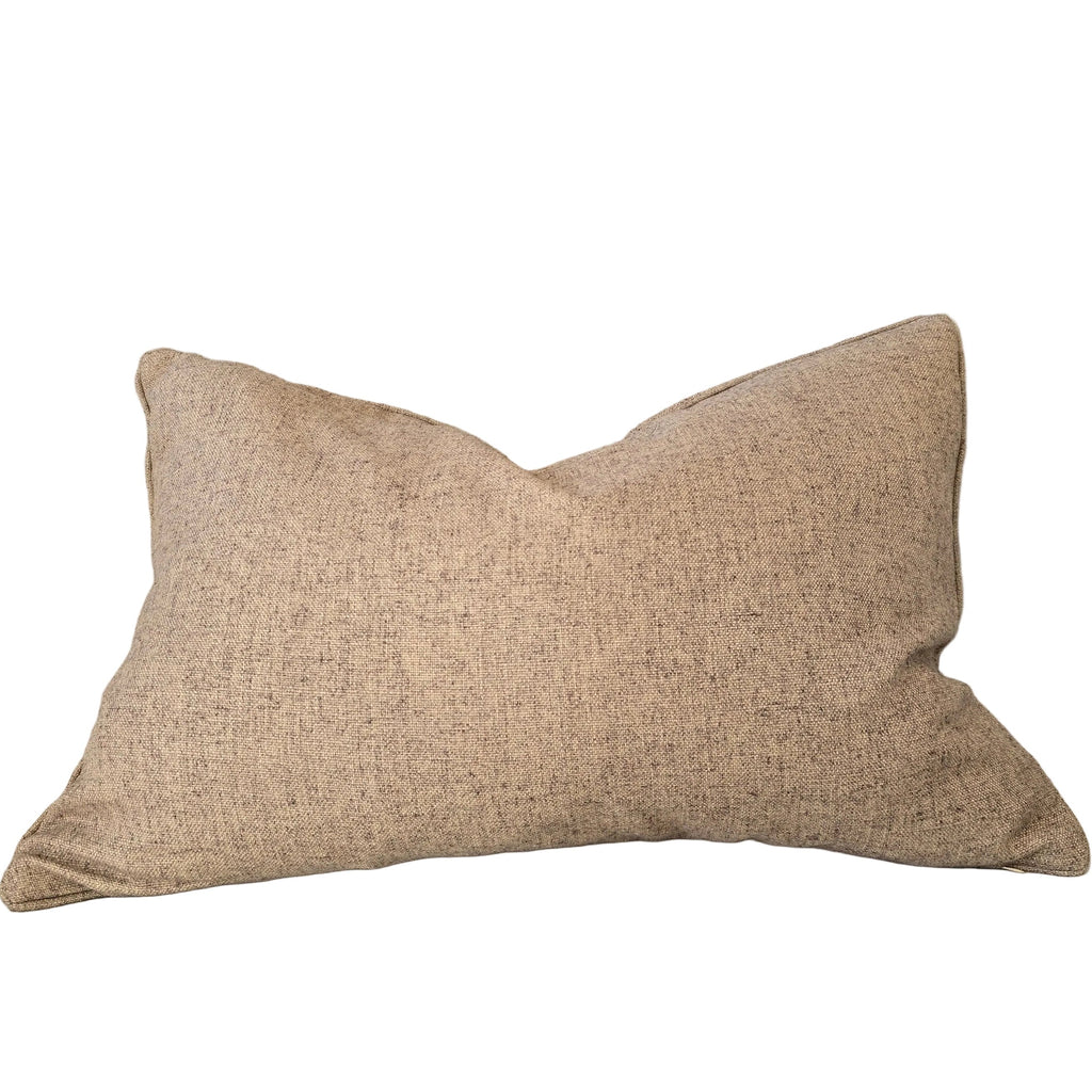 A rectangular beige textured throw pillow resting on a light beige upholstered sofa, with a wooden shelf and decorative objects partially visible on the left.