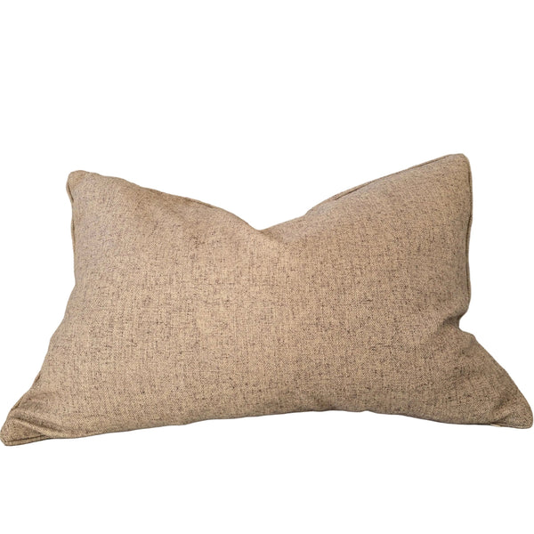 A rectangular beige textured throw pillow resting on a light beige upholstered sofa, with a wooden shelf and decorative objects partially visible on the left.