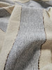 Close-up of a woven textile with vertical stripes in light gray and warm cream, showing the texture and stitching details.